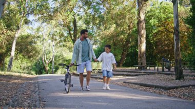 Bisikletli bir çocuk gün ışığı yolunda yürüyor. Pozitif aile yürürken el ele tutuşup konuşuyor. Bisikletli sakallı baba orman manzarasında küçük oğluyla eğleniyor. Ebeveynlik kavramı