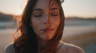 Gün batımında dinlenen portre modeli yumuşak bir rüzgar estirdi. Şehvetli bir kadın gözlerini kapatıyor ve sahilde sakin bir akşamın tadını çıkarıyor. Altın gün doğumunda poz veren güzel bayan huzuru hissediyor..