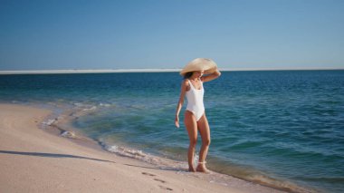 Hasır şapka takmış, dalgalara basan rahat bir bayan. Kaygısız kadın gezgin turkuaz okyanus suyuyla yıkanmış güzel kumsalda yürüyor. Zarif esmer kız adada mutlu yaz tatilleri..