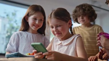 Gülümseyen öğrenciler okul tatilinin tadını çıkarıyorlar. Sınıfta sınıf arkadaşlarıyla akıllı telefondan oynayan mutlu bir öğrenci. Sınıfta cep telefonuyla etkileşime giren neşeli çocuklar.