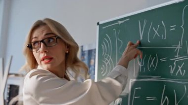 Gülümseyen hoca üniversite sınıfında cebir denklemleri öğretiyor. Tahtada matematik formülleri gösteren pozitif kadın öğretmen bilinmeyen öğrencilerle konuşuyor. Gözlüklü kadın eğitmenin dersi var..