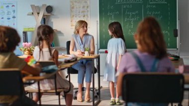 Öğretmen, sınıfın tahtasında duran küçük kızla etkileşim halinde. Kara tahtada cevap veren tatlı bir kız öğrenci. Genç bayan öğretmen sınıf odasında öğrencinin konuşmasını dinliyor. İlkokul eğitimi.