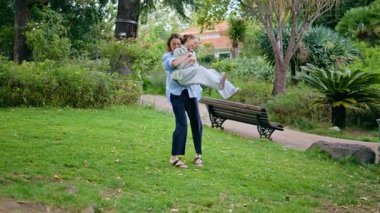 Green Park 'ta dönen neşeli bir anne. Gülümseyen bebek bakıcısı bahçede oynayan tatlı bir kızı elinde tutuyor. Güzel anne, neşeli kız, bereketli doğada birlikte eğleniyor. Sevgi dolu aile ilişkisi