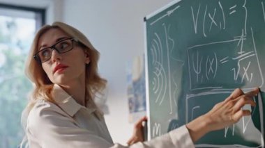 Sınıfın tahtasında yazan cebir teorisini açıklayan kadın. Sınıfta fizik denklemlerini gösteren gözlük takan zeki kadın öğretmen. Ciddi kadın eğitmen, okulda matematik dersi veriyor..