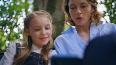 Green Doğa Merkezi 'nde cep telefonu izleyen sevimli bir aile. Meraklı anne, komik kız cep telefonuyla iletişim kurmaktan zevk alıyor. Küçük bir kız çocuğu ağacın altında oturuyor.