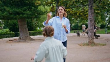 Aile, park yürüyüşünde renkli sabun köpükleri oynuyor. Mutlu kadın, anne, tatlı kız, yeşillik doğasında dinlenirken birlikte vakit geçirmeyi seviyor. Neşeli çocuk anne eğleniyor. Tatlı çocukluk anı konsepti 