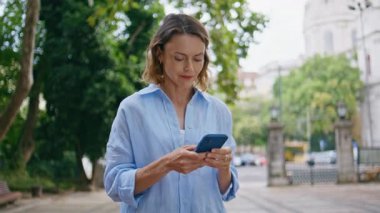 Ciddi görünümlü bir bayan, yaz parkında tek başına dikiliyor. Sakin bir caddede elinde akıllı telefonla bekleyen rahat bir kadın. Şehir merkezinde cep telefonu gezdirme yolu olan bir yetişkin modeli 