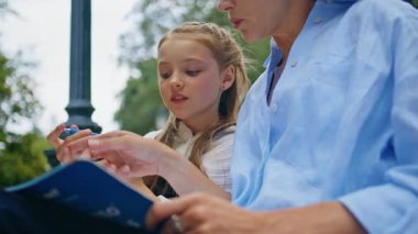 Kapanış okullu kız parkta annemle konuşuyor. Küçük şirin çocuk kitap yazıyor ve kadın ebeveynlerle ahşap bankta ders çalışıyor. Pozitif meraklı çocuk kitabı gibi sorular soruyor. Aile kavramı