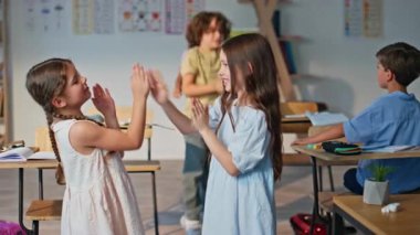 Mutlu liseli kızlar sınıfın içinde el çırpıyorlar. İki ilkokul öğrencisi okul tatilinde oyun oynuyor. Neşeli kızlar sınıf masasına oturur öğretmenle derslere başlarlar..