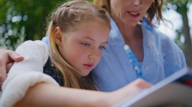 Kapalı okul kızı. Yeşillikte annemle ödev yaparken defter yazıyor. Düşünceli gülümseyen çocuk ev ödevlerini okuyor cevapları annesinin yardımıyla dolduruyor. Önemseyen bir kadın küçük kızını kucaklıyor.