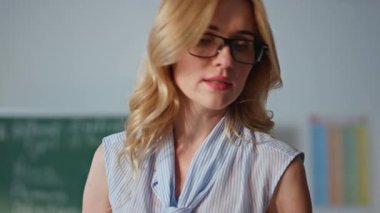 Kapanış öğretmeninin rehber defteri öğrenci katılımını kontrol ediyor. Gözlüklü genç bayan eğitimci öğrencilere eğitim kitabı okuyor. İlkokul öğretmenliği yapan profesyonel bir bayan öğretmen.