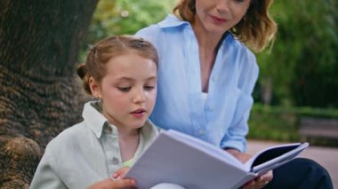 Küçük çocuk, anne için parkta peri masalı okuyor. Kadın ebeveyn ve çocuk, yaz bahçesinde kitap okuyorlar. Önemseyen anne-kız yakınlaşması aile hafta sonu yaşam tarzı 