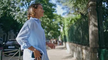 Neşeli bir kadın güneş ışığı sokağına el sallıyor. Annesinin okul çantasıyla küçük kızıyla tanışmasına çok sevindi. Sevimli bayan ebeveyn, küçük çocuğu seviyor. Yeşillik caddesinde kucaklaşıyorlar.