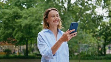 Kadınlar şehir parkında yürürken görüntülü konuşmalardan hoşlanırlar. Yeşil caddede konuşan gülümseyen kadın cep telefonu. Kaygısız bayan akıllı telefonları karşılıyor. Şehir merkezinde tek başına geziniyor. İletişim konsepti 
