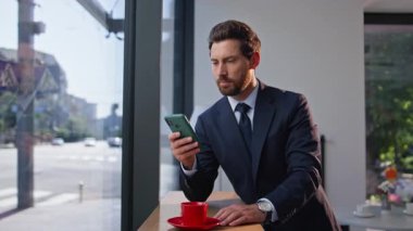 Gülümseyen işletme sahibi cep telefonuna mesaj atıyor. Şehir restoranında kahvenin tadını çıkarıyor. Mutlu iş adamı espresso içiyor. Akıllı telefon gibi görünüyor.