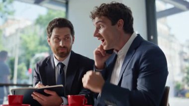 İş arkadaşları panoramik restoranda iş görüşmesi yapıyor. Gülümseyen iş arkadaşları, modern kafede başarılı olmak için akıllı telefonlardan bahsediyorlar. Mutlu yöneticiler telefonda birlikte çalışarak harika haberler duyuyorlar.