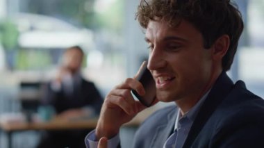 Şirket çalışanı, hafif iş portresindeki akıllı telefondan bahsediyor. Gülümseyen iş adamı, Panoramik Ofis 'te haberleşen meslektaşı olarak harika haberleri paylaşıyor. İki iş arkadaşı cep telefonlarını birlikte arıyor.