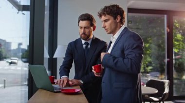 Endişeli iş adamları panoramik kafede şirket sorunlarını konuşurken dizüstü bilgisayara bakıyorlar. İnternette birlikte çalışan iki yönetici öğle yemeği molasında büyük pencere ofis lobisini tartışıyorlar.