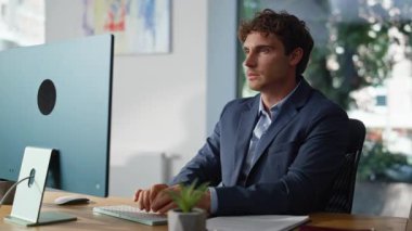 Bilgisayarda ciddi bir yönetici e-postası yazıyor. Organize ofis işyerinde oturuyor. Yakın plan. Klavyeyle çalışan odaklanmış iş adamı görev üzerinde düşünüyor. Çalışma alanında çevrimiçi proje geliştiren yakışıklı yönetici