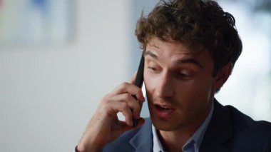 İş yerinde cep telefonuyla konuşan, evraklara bakan yakın bir adam. Gülümseyen iş adamının portresi. Omzuyla akıllı telefonu tutuyor. Genç adam cep telefonuyla iş görüşmeleri yapıyor.