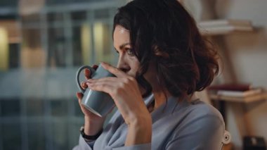 Akşam acentesinde kahve içen bir iş kadını. Yakın plan. Portre ciddi kadın CEO modern ofiste iş molalarında sıcak içecekten hoşlanır. Bardaklı bayan patron iş geliştirmeyi düşünüyor.