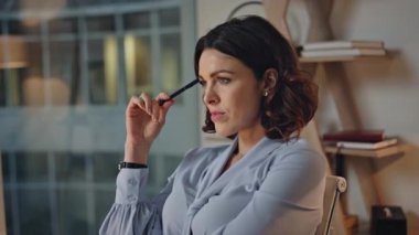 Akşamları iş yerinde elinde kalem tutan düşünceli bir kadın. Karanlık modern ofiste düşünceli bir yönetici iş stratejisi planlıyor. İş kadını iş konularında fazla mesai yapmayı düşünüyor.