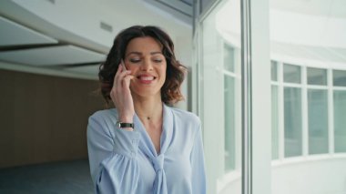 Kendine güvenen bayan patron cep telefonu şirketini arıyor. Zarif bluzuyla gülümseyen iş kadını akıllı telefondan konuşuyor. Başarılı kadın CEO yönetici koridorda cep telefonuyla konuşuyor.