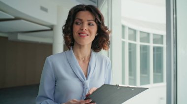 Gülümseyen patron modern ofiste dokümanları gözden geçiriyor. Kendine güveni olan kadın yönetici iş anlaşmasıyla iş arkadaşını selamlıyor. Mutlu kadın yönetici koridor penceresinin yanında kağıtlara bakıyor..