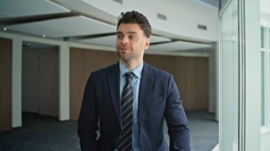 Kendine güvenen iş adamı modern ofiste şık bir takım elbiseyle dolaşıyor. Arkadaş canlısı erkek yönetici şirket ortamında bilinmeyen meslektaşlarını selamlıyor. Mutlu girişimci şirket koridoruna çıkıyor..