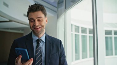 Gülümseyen işadamı cep telefonu çağrılarına cevap veriyor. Ofis koridoru kapalı. Başarılı bir yönetici akıllı telefondan konuşuyor. Kendine güvenen yönetmen şirket koridorunda keyifli bir telefon görüşmesi yapar..