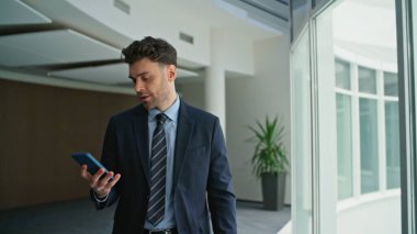 Patron panoramik pencerelerin yakınındaki şirket ofisinden çağrıya cevap veriyor. Şirket koridorunda gülümseyen profesyonel bir yönetici akıllı telefondan konuşuyor. Güvenilir yöneticinin dost canlısı cep telefonu konuşması var.