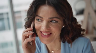 Çalışanlar şirket içi yakın plan akıllı telefon konuşmalarından hoşlanırlar. Gülümseyen kadın ofisteki cep telefonunu arayıp iyi haberleri paylaştı. İş kadını modern işyerindeki telefon konuşmalarında iş fikrini tartışıyor.