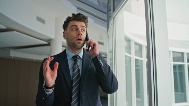 Endişeli yönetici cep telefonunu arıyor ofis koridorunu kapatıyor. Duygusal iş adamı iş hatasını akıllı telefon konuşmalarıyla açıklıyor. Memnun olmayan erkek patron iş sorunundan şikayetçi..