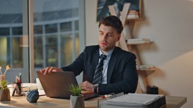 Tükenmiş yönetici akşam iş yerindeki bilgisayarı kapatıyor. Yorgun işadamı, modern ofiste bitkin düşerek işini bitirdi. İş yeri lambasında oturan çok çalışan şirket uzmanı..