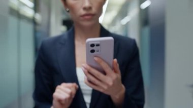 İş kadını parmakları cep telefonuna dokunuyor şirket koridorunda yürüyor yakın plan. Başarılı bayan uzman akıllı telefonları tarayıp boş koridora gidiyor. Kadın CEO cep telefonu ekranını araklıyor SMS açıyor