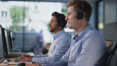 Modern çağrı merkezinde çalışan müşteri hizmetleri ekibi yakın çekimde. Yardım masası çalışanları açık alandaki iş yerinde kulaklıkla konuşuyorlar. Grup telesale yöneticileri satış öneren müşterilere danışıyor