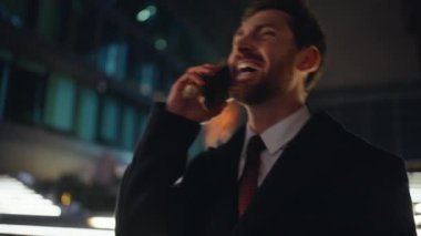 Gülümseyen işadamı, akşam vakti akıllı telefondan konuşuyor. Neşeli yakışıklı adam cep telefonu iletişimine gülüyor. Mutlu traşsız yönetmen olumlu sohbetin tadını çıkarıyor. 