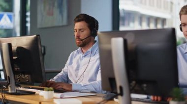 Bilgisayarların başında çalışan iletişim merkezi ekibi açık uzay ofisindeki kulaklıklardan bahsediyor. Hizmet masası çalışanları modern işyerlerinde online danışmanlık yapıyorlar. Profesyonel destek sağlayan yardım masası operatörleri.