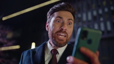 Akşam kazananı Dark Square Portre 'de cep telefonu ekranını okuyor. Çok neşeli sakallı bir çalışan akıllı telefona bakıyor ve gece şehrinde başarılar diliyor. Resmi takım elbiseli heyecanlı adam işten sonra piyango kazanıyor.