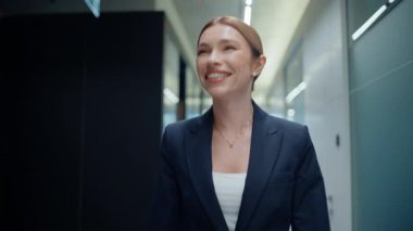 Arkadaş canlısı ofis müdürü iş arkadaşlarını selamlıyor. Yakın çekim yap. Gülümseyen iş kadını, gri modern salonda tek başına dolaşırken başarısını gösteriyor. Kendine güvenen iş kadını, şirket toplantısına giden röntgenci dolaplar.