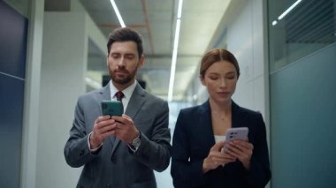 İş kadını iş kadını koridorda yürürken akıllı telefonları yakın çekim yapın. İki şirket çalışanı mesajlaşan cep telefonlarını bozuyor. Gülümseyen profesyoneller boş salonda vakit geçiriyorlar.