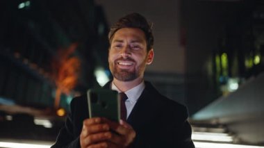 Akşam ışıkları önünde telefon mesajı okuyan mutlu adam portre çiziyor. Gülümseyen iş adamı akıllı telefon ekranına bakıyor ve gece tek başına duruyor. Dark City 'de dijital aygıt tutan yakışıklı yönetici 