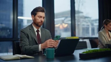 Akşam müdürü yakın plan çekimde akıllı telefon panoramik pencereleri okuyor. Rahatlayan meslektaşlar cep telefonlarına göz gezdiriyorlar karanlık iş yerinde yakın plan çekimde mola veriyorlar. İki ofis çalışanı lamba ışığında aletler kullanıyor.