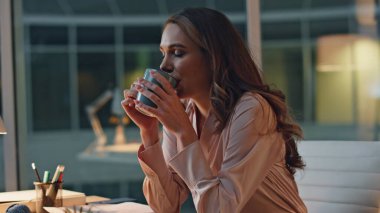 Profesyonel kadın gece ofisinde mola veriyor. İşten sonra kahve içen, rahatlayan bir kadın. Gülümseyen sakin yönetici masasında sükunetin keyfini çıkartıyor. İşçi çayını yudumluyor