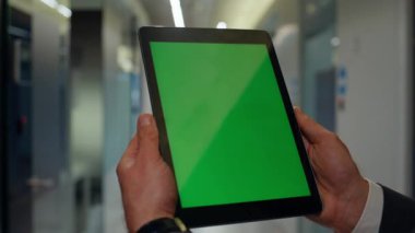 Yeşilekran tablet okuma ödevlerini tutan eller yakın çekime gitsin. Bilinmeyen adam ofis binasındaki bilgisayardan programı izliyor. Krom anahtar aygıtı kullanan bir iş adamı içeride vakit geçiriyor