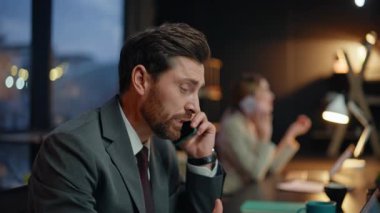 Gece vardiyasında cep telefonuyla konuşan bir masa başı çalışanı. Müşterilerle iletişim kuran iki pazarlama uzmanı akşam çalışma alanında birbirlerine gülümseyerek bakıyorlar.
