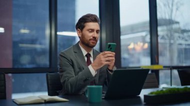 Pozitif iş adamı panoramik akşam iş yerinde akıllı telefon mesajları gönderiyor. Rahat iş arkadaşları cep telefonlarıyla dinleniyor ve karanlık kabinede mola veriyorlar. İki iş arkadaşı birbirine gülümsüyor.