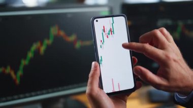 Borsa haritalarının finansal verilerini gösteren akıllı telefonları tutan tüccar elleri. Grafik para piyasasını analiz eden tanınmamış bir işadamı. Adam broker yatırım şirketinde cep telefonu uygulamasına göz atıyor