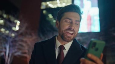 Duygusal iş adamı, akşam vakti kameralı telefondan konuşuyor. Aşırı neşeli yakışıklı adam cep telefonu iletişiminde başarıyı paylaşıyor. Mutlu yönetmen internette olumlu sohbetten hoşlanıyor