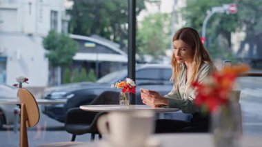 Modern restoranda akıllı telefon saatine bakan dalgın bir bayan bekliyor. Kafeterya masasında tek başına oturan düşünceli güzel bir kadın. Çekici bayan sarışın rahat bir kafede dinleniyor ve yalnız hissediyor..